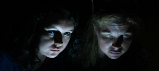 Light painting of 2 women's faces lit from below, in front of a black background